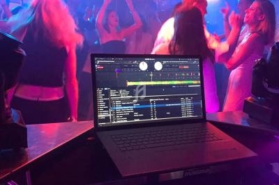 Vue d'une piste de danse animée depuis une table de DJ avec un ordinateur portable affichant un logiciel de mixage.