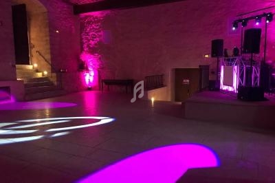 Salle en pierre éclairée par des lumières roses et violettes, avec une scène équipée de matériel de sonorisation.