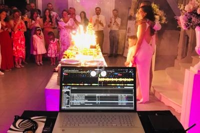 Vue depuis une table de DJ sur une fête avec des invités rassemblés autour d'un gâteau illuminé par des bougies.