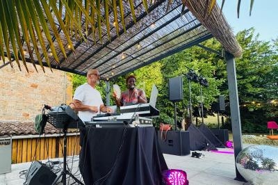 Deux personnes animent une soirée en extérieur sous une pergola, avec des équipements de DJ et des lumières colorées.