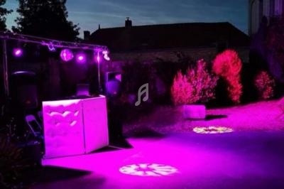 Installation de DJ en extérieur avec éclairage violet et projecteurs lumineux, entourée de végétation et bâtiments en…