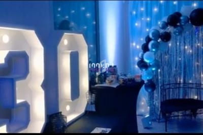 Décoration d'anniversaire avec chiffres lumineux ’30’, arche de ballons noirs et argentés, et fond lumineux.