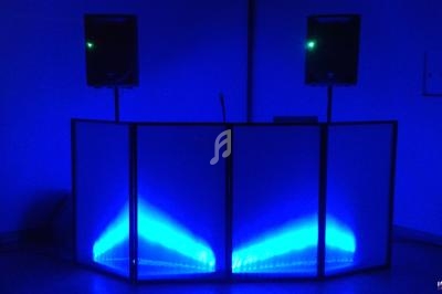 Console de DJ éclairée par des lumières bleues, entourée de deux enceintes sur pieds dans une pièce sombre.