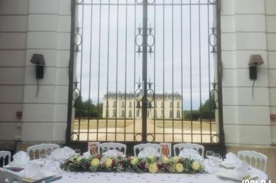 Table décorée avec des fleurs et vaisselle, placée devant une grille en fer forgé avec un château en arrière-plan.