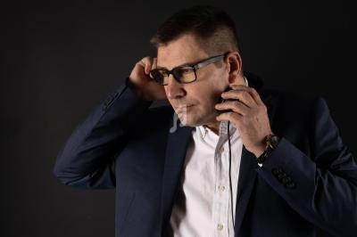 Homme en costume bleu et chemise blanche ajustant un casque audio, sur fond noir.