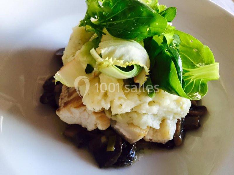 Plat composé de poisson, purée de pommes de terre, champignons et feuilles de salade verte sur une assiette blanche.