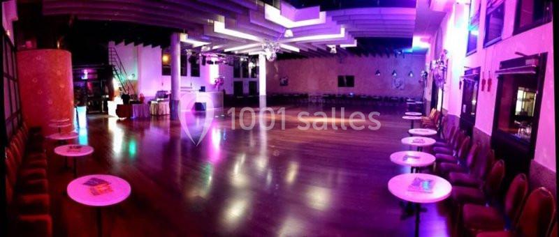 Salle de danse spacieuse avec parquet brillant, tables rondes alignées et éclairage coloré tamisé.