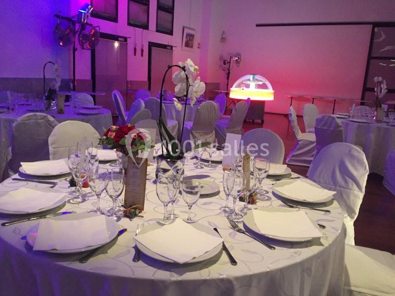 Salle de réception décorée avec des tables rondes dressées, nappes blanches et éclairage tamisé.