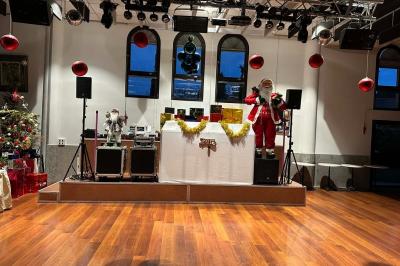 Salle décorée pour Noël avec une scène équipée de matériel audio, des décorations festives et une statue du Père Noël.