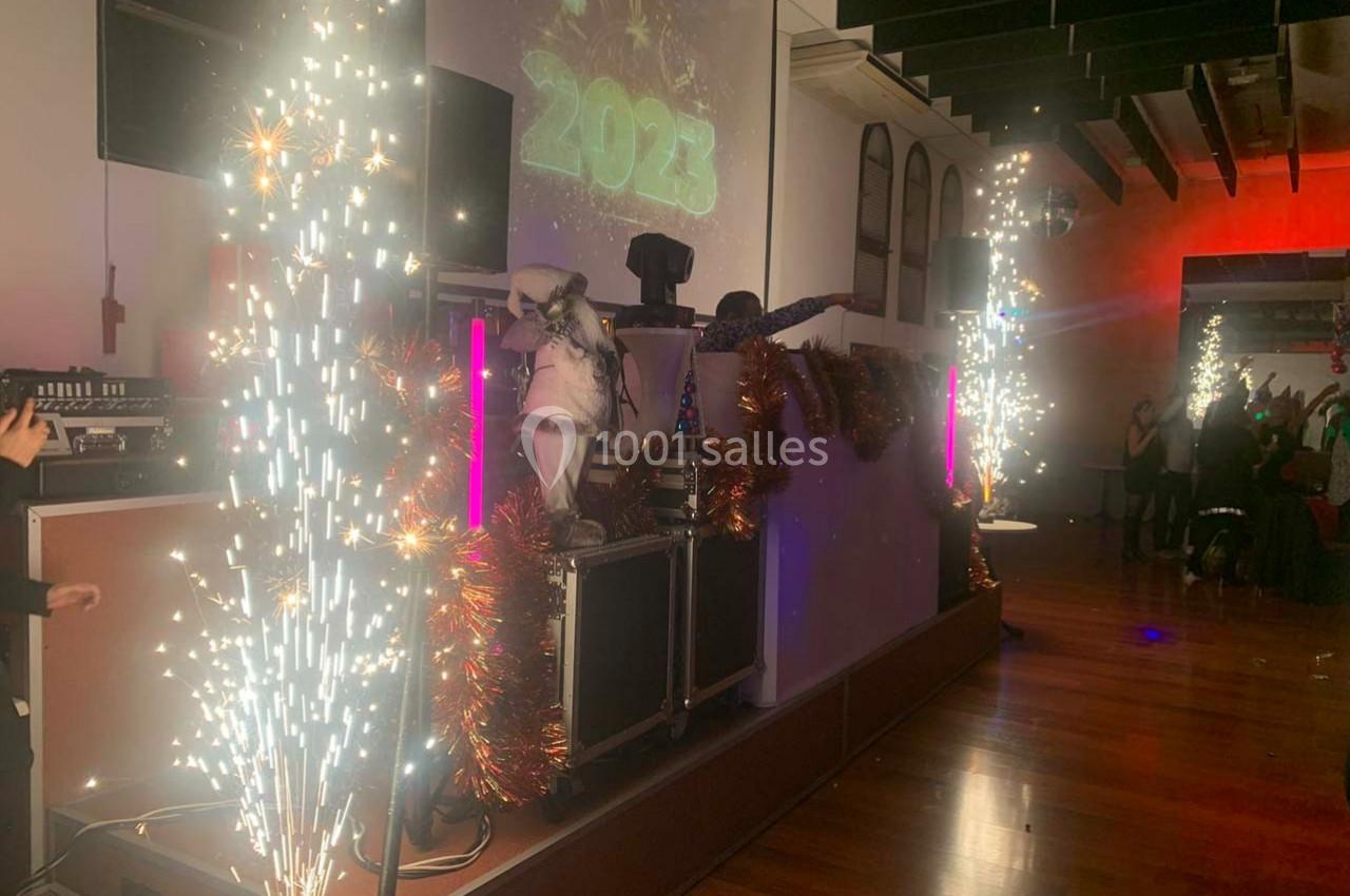 Scène festive avec DJ, décorations lumineuses, étincelles et projection de ’2023’ dans une salle animée.
