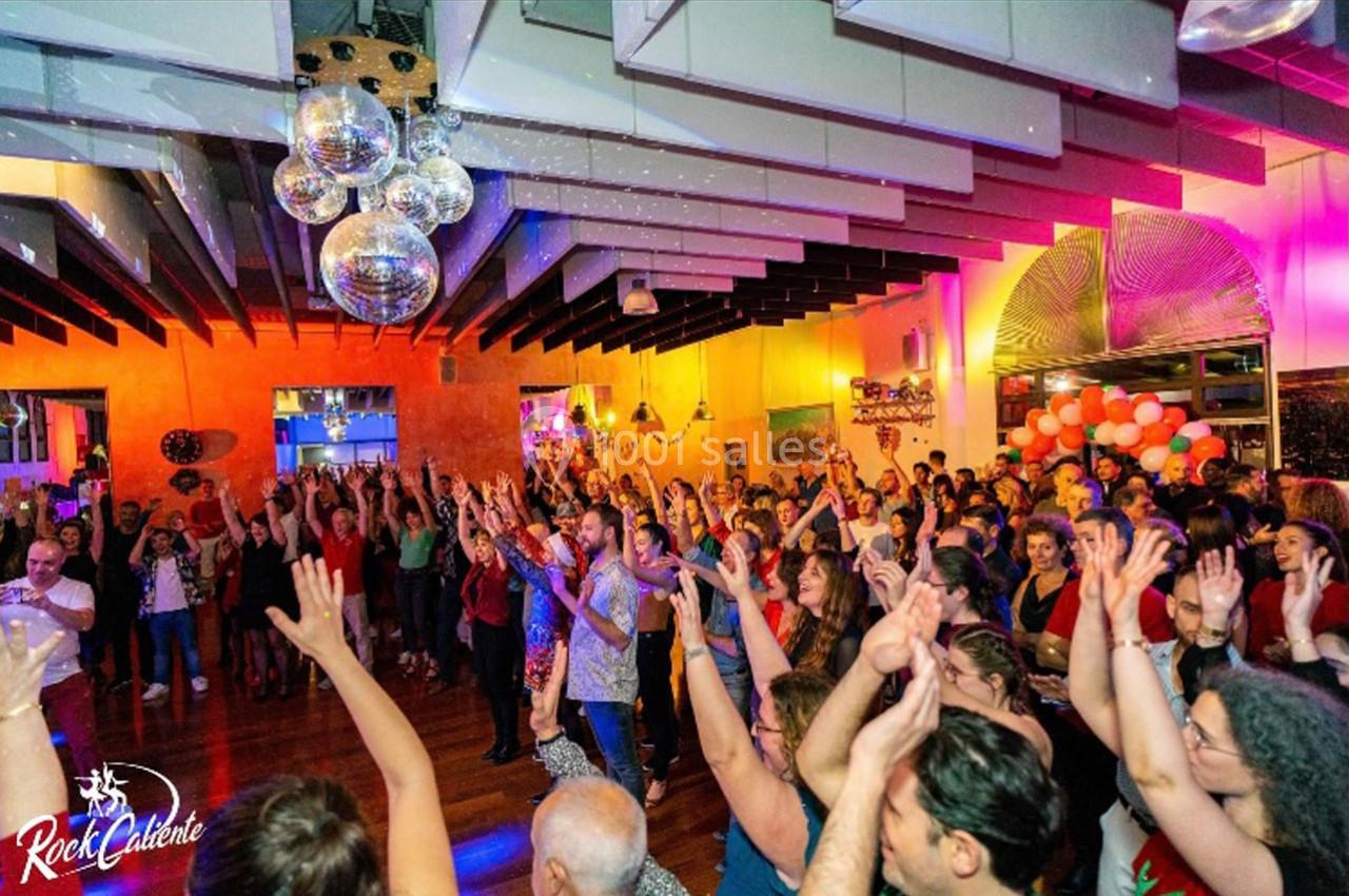 Groupe de personnes levant les bras lors d'un événement festif dans une salle décorée avec des lumières et des boules disco.