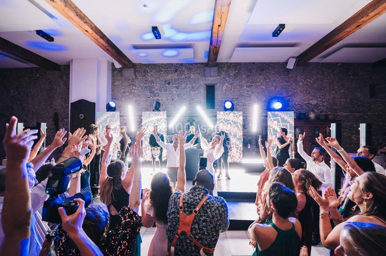 Groupe de personnes dansant et levant les bras lors d'une fête avec éclairages colorés et musique en direct.