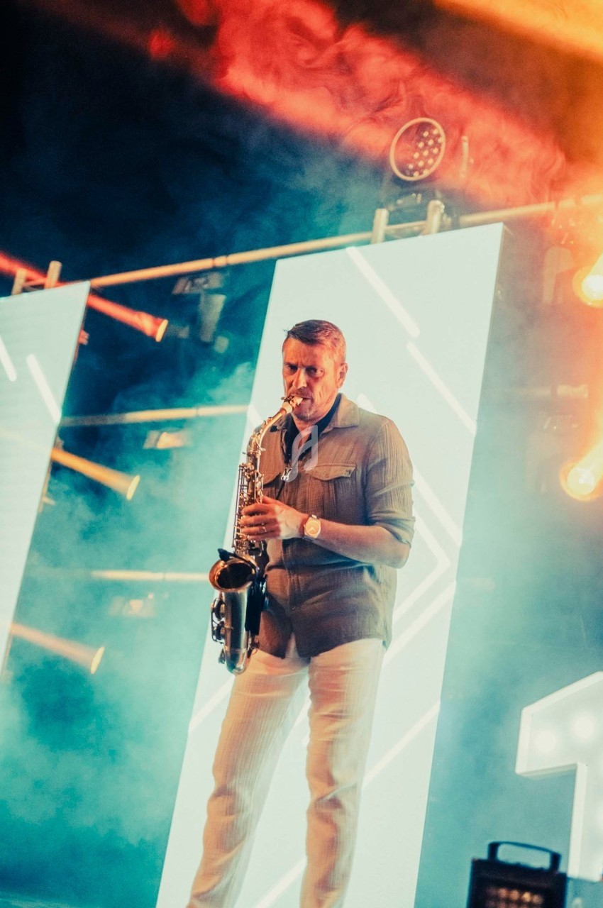 Un musicien joue du saxophone sur une scène illuminée par des panneaux lumineux et des projecteurs colorés.