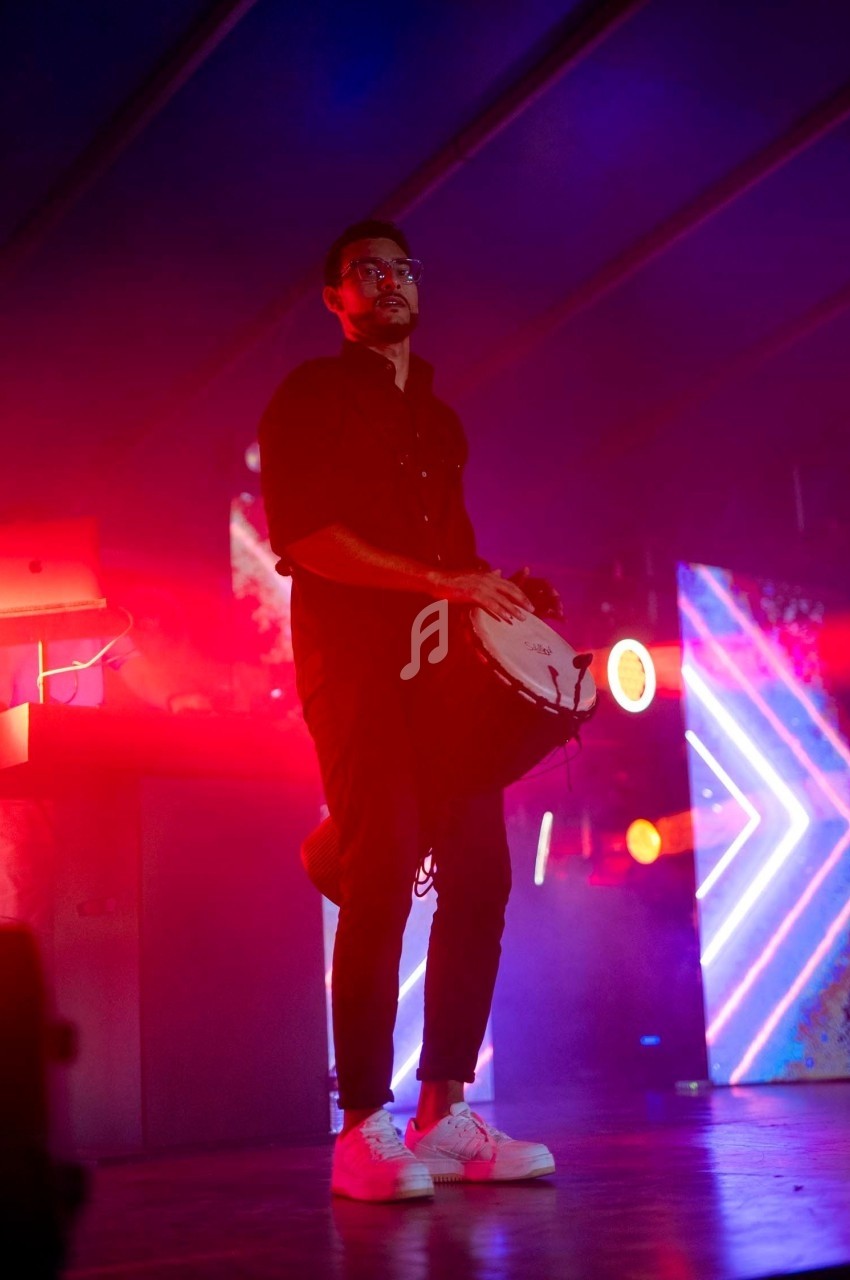 Un musicien joue du tambourin sur une scène éclairée par des lumières rouges et bleues.