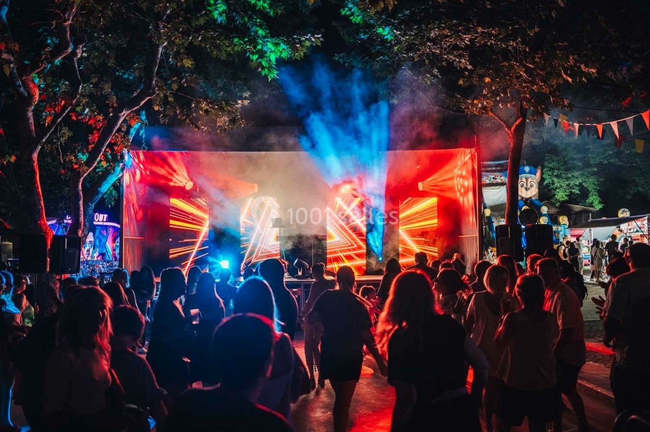 Foule rassemblée devant une scène illuminée par des jeux de lumière rouges et bleus lors d'un événement en plein air.