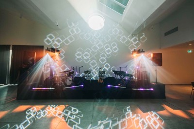 Plateforme circulaire avec un anneau lumineux sur pied, installée sur une pelouse devant un mur en pierre couvert de lierre.