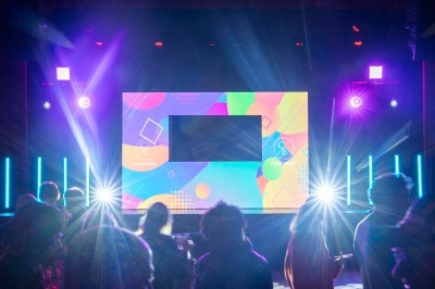 Plateforme circulaire avec un anneau lumineux sur pied, installée sur une pelouse devant un mur en pierre couvert de lierre.