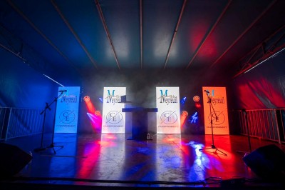 Plateforme circulaire avec un anneau lumineux sur pied, installée sur une pelouse devant un mur en pierre couvert de lierre.