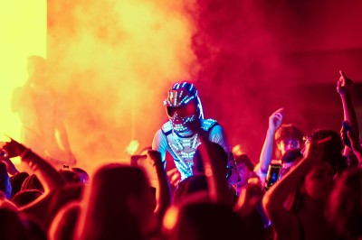 Plateforme circulaire avec un anneau lumineux sur pied, installée sur une pelouse devant un mur en pierre couvert de lierre.