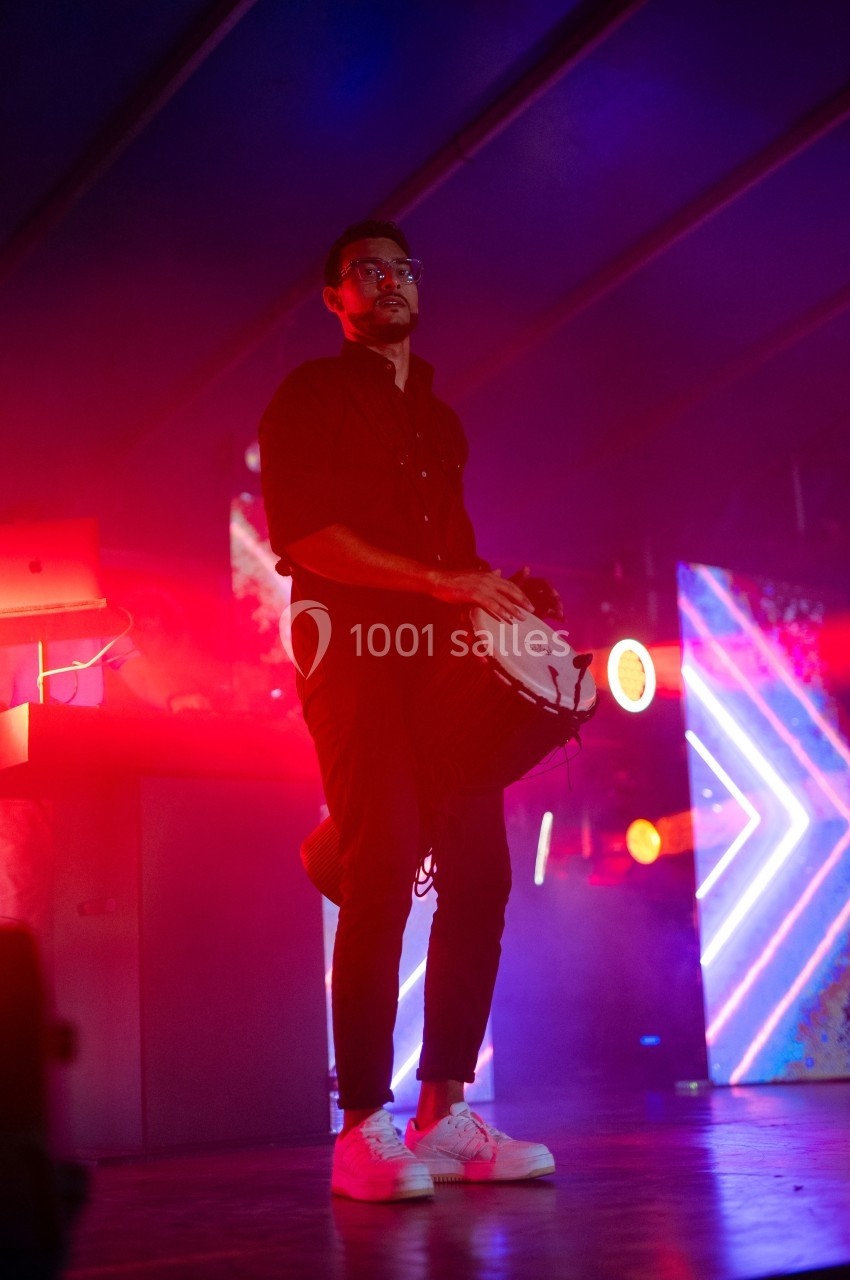 Un musicien joue du tambour sous un éclairage coloré dans une ambiance de scène.