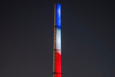 Plateforme circulaire avec un anneau lumineux sur pied, installée sur une pelouse devant un mur en pierre couvert de lierre.