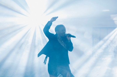Plateforme circulaire avec un anneau lumineux sur pied, installée sur une pelouse devant un mur en pierre couvert de lierre.