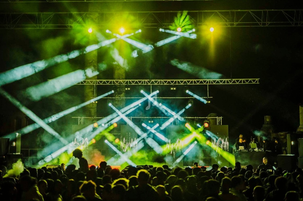 Foule devant une scène illuminée par des projecteurs colorés lors d'un concert nocturne.
