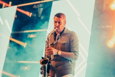 Plateforme circulaire avec un anneau lumineux sur pied, installée sur une pelouse devant un mur en pierre couvert de lierre.