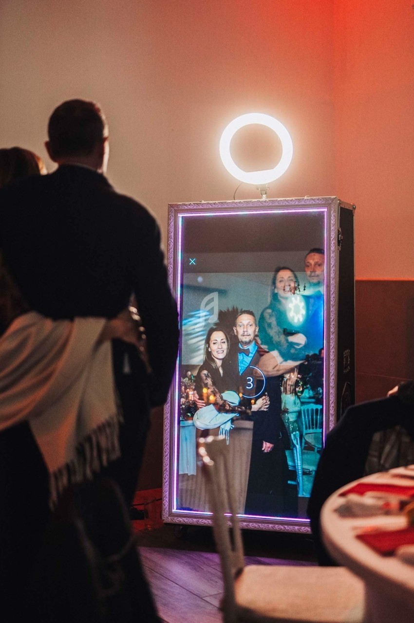Un groupe de personnes se prend en photo devant un miroir interactif éclairé par une lampe circulaire.