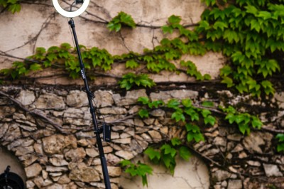 Plateforme circulaire avec un anneau lumineux sur pied, installée sur une pelouse devant un mur en pierre couvert de lierre.