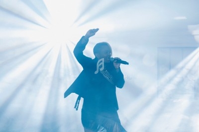 Une chanteuse sur scène, éclairée par des faisceaux lumineux dans une ambiance enfumée.