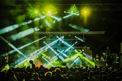 Foule devant une scène illuminée par des faisceaux lumineux colorés lors d'un concert nocturne.