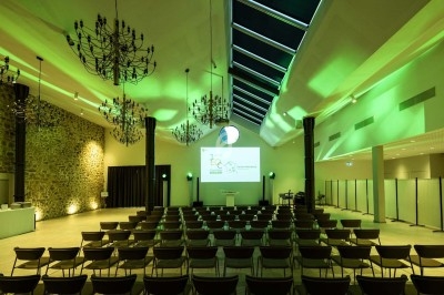 Salle de conférence avec rangées de chaises, écran de projection allumé et éclairage vert diffus.