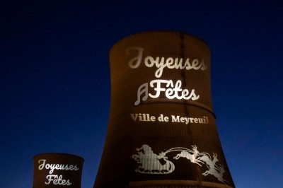 Tours de refroidissement illuminées par des projections de vœux de fêtes et de motifs festifs, de nuit.