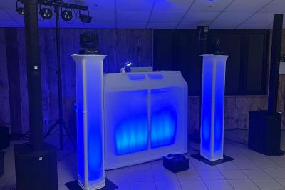 Scène décorée avec guirlandes lumineuses, plantes et une table de DJ éclairée en bleu et blanc.