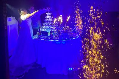 Scène décorée avec guirlandes lumineuses, plantes et une table de DJ éclairée en bleu et blanc.