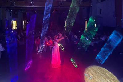 Scène décorée avec guirlandes lumineuses, plantes et une table de DJ éclairée en bleu et blanc.