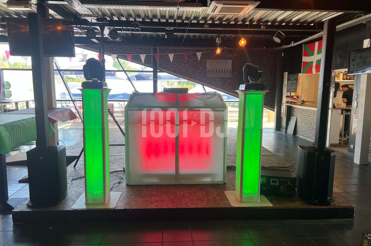 Stand de DJ avec éclairage LED rouge et vert, installé dans une salle avec décoration intérieure et lumière naturelle.