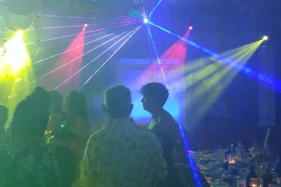 Scène décorée avec guirlandes lumineuses, plantes et une table de DJ éclairée en bleu et blanc.