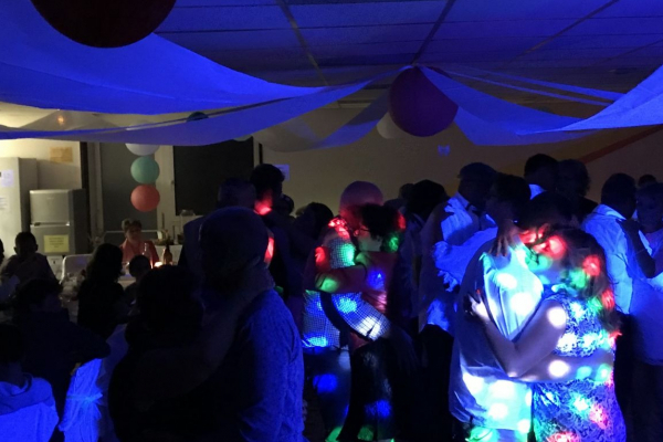 Des personnes dansent sous des lumières colorées dans une salle décorée avec des rubans et des ballons.