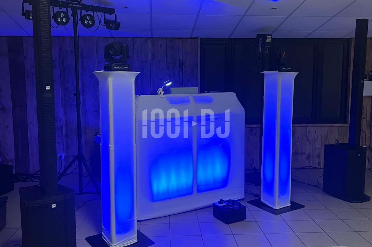 Poste de DJ éclairé en bleu avec deux colonnes lumineuses, matériel audio et projecteurs dans une salle.