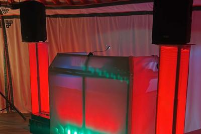 Stand de DJ avec éclairage LED rouge et vert, installé dans une salle avec décoration intérieure et lumière naturelle.