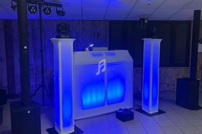 Poste de DJ éclairé en bleu avec deux colonnes lumineuses, matériel audio et projecteurs dans une salle.