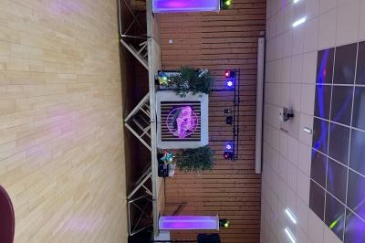 Scène de spectacle avec éclairage coloré, décorations végétales et équipement audio sur un sol en parquet.