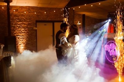 Un couple danse dans une salle éclairée par des lumières colorées, des étincelles et une machine à fumée.