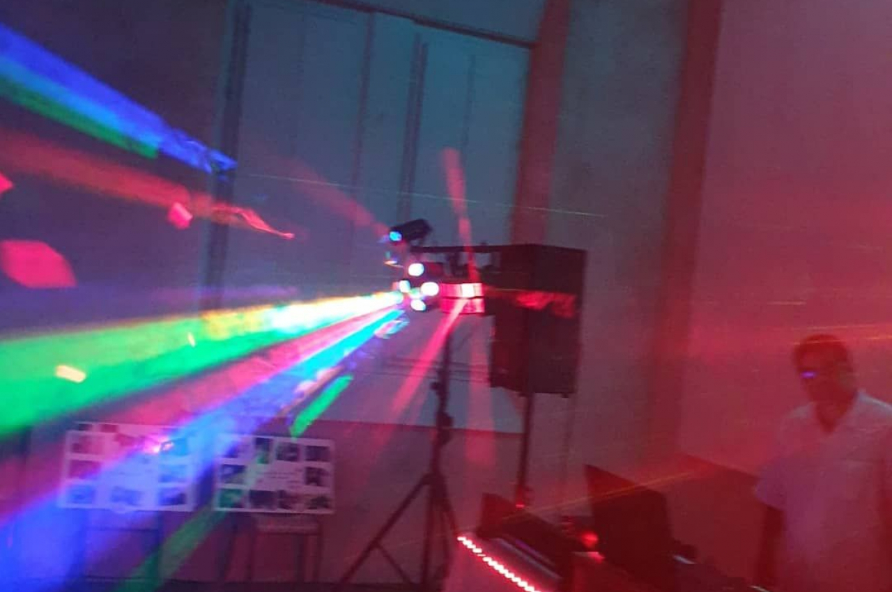 Effets lumineux colorés projetés dans une salle sombre avec un DJ et son équipement à droite.