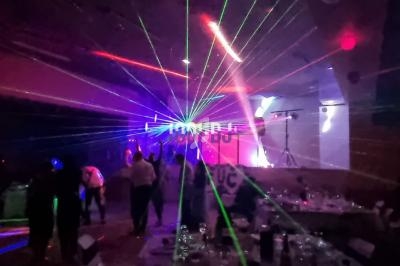 Des personnes dansent dans une salle sombre éclairée par des faisceaux lumineux colorés et des effets laser.