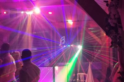 Des faisceaux lumineux colorés illuminent une salle avec des personnes debout dans une ambiance festive.