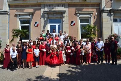 Groupe de personnes posant devant un bâtiment marqué ’Hôtel de Ville’, certaines en tenue habillée rouge et blanche.
