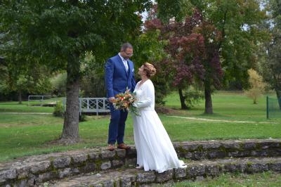 Un couple en tenue de mariage se tient sur des marches en pierre dans un parc verdoyant avec des arbres en arrière-plan.